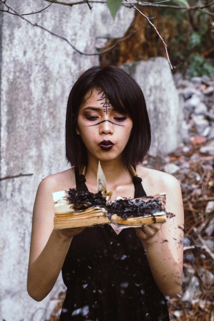 Young woman performing witchcraft ritual with burning book outdoors.