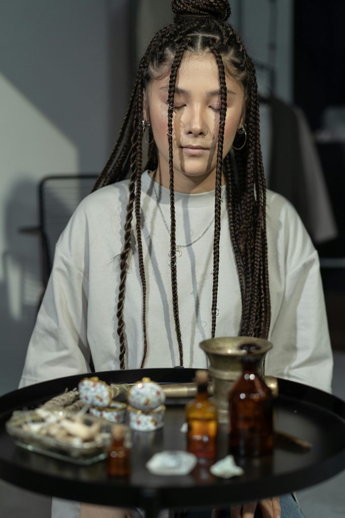 Young woman with braids in a mystical ritual setting, eyes closed, indoors.